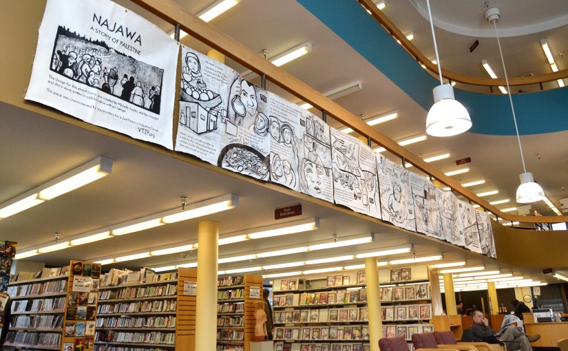 Photo taken at the installation of "Najawa: A Story of Palestine" in Burlington, VT's Fletcher Free Library. The full comic is in view, hanging from a second-story banister.