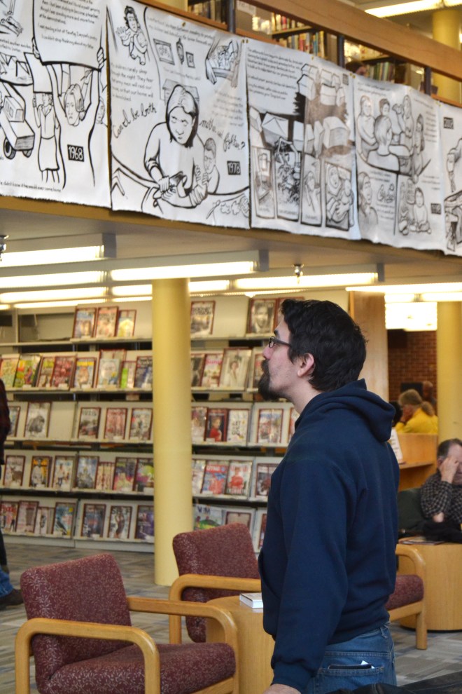Photo taken at the opening of "Najawa: A Story of Palestine" in Burlington, VT's Fletcher Free Library. A young man looks up to where the comic hangs from a second-story banister.