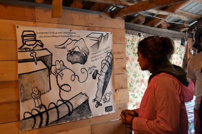 Photo of a woman in a pink raincoat viewing the Najawa installation at Bread & Puppet.